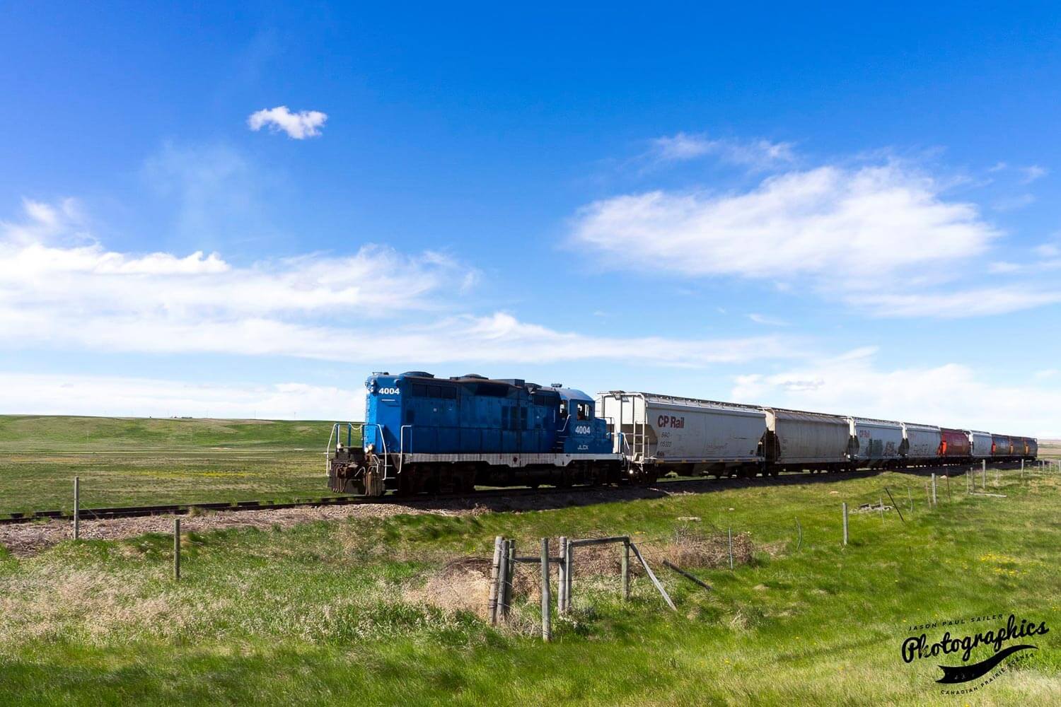 Blue train pushing railroad cars through a the prairies